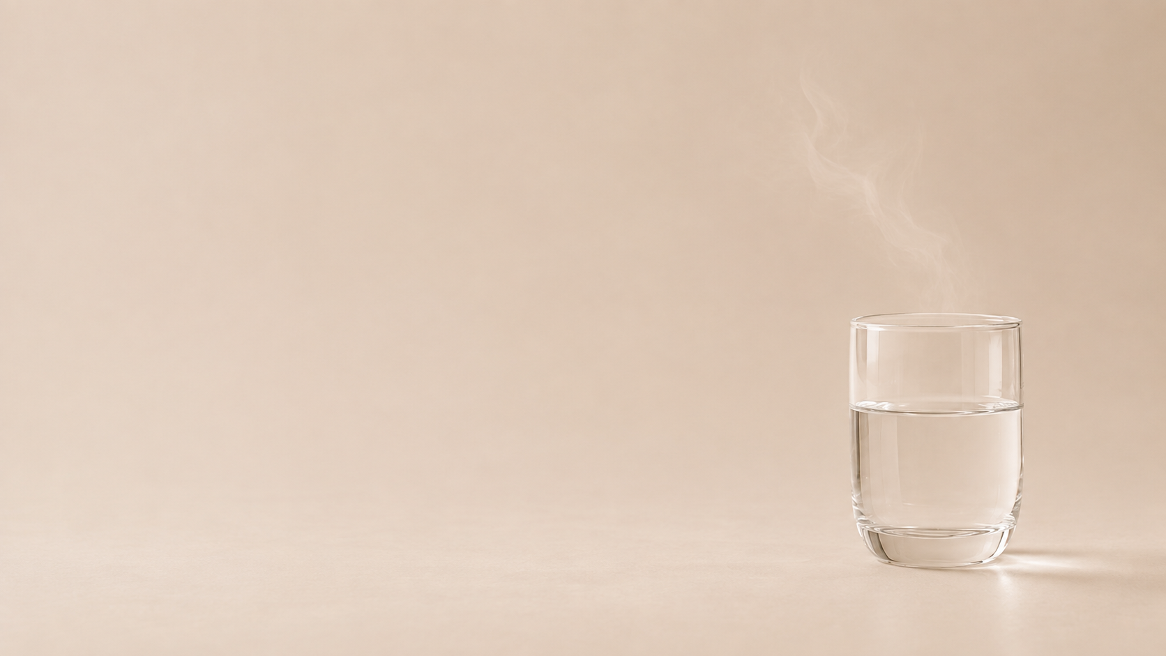 A glass of water with rising steam on a warm sandstone surface.